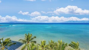 Une plage tropicale aux eaux turquoise et limpides, bordée de palmiers, avec une chaîne de montagnes qui se dessine à l’horizon.