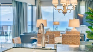 Une salle de bain moderne avec un robinet élégant, un comptoir en marbre et une vue sur l’espace de vie, où se trouvent un canapé et des lampes.