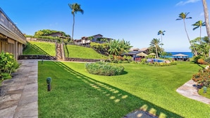 Une pelouse bien entretenue, avec un chemin de pierres menant à un bâtiment, le tout entouré d’une végétation tropicale et offrant une vue dégagée sur l’océan.