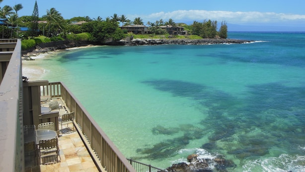 Une propriété située en bord de mer, dotée d’une terrasse en bois et d’un espace salon extérieur, offrant une vue imprenable sur des eaux turquoise et une côte rocheuse bordée d’une végétation luxuriante.