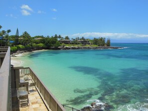 Une propriété située en bord de mer, dotée d’une terrasse en bois et d’un espace salon extérieur, offrant une vue imprenable sur des eaux turquoise et une côte rocheuse bordée d’une végétation luxuriante.
