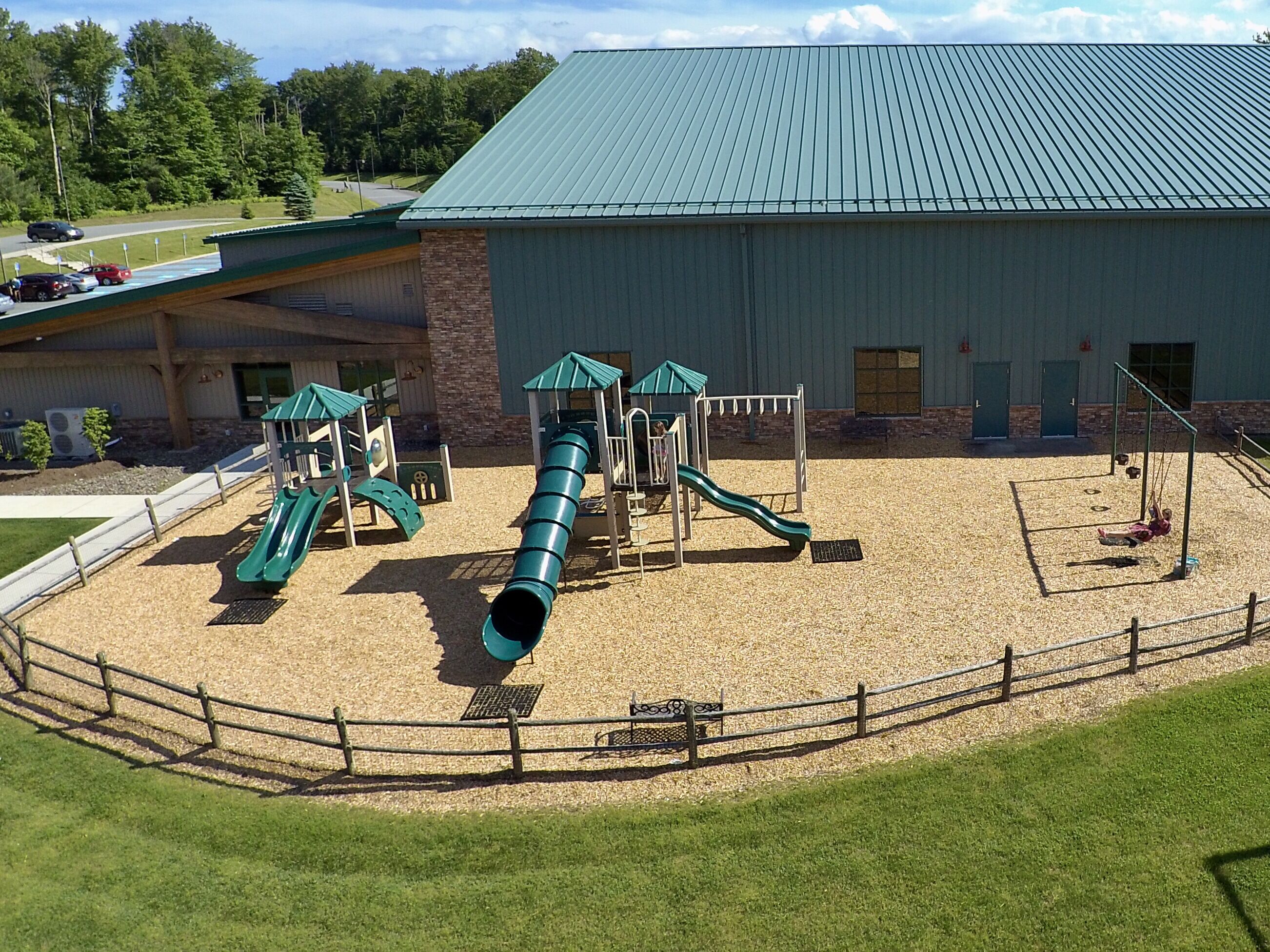 A playground with slides and climbing structures, surrounded by a fenced area with a building in the background.
