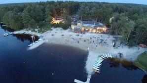 An aerial view of a lakeside property with a dock, a building with multiple windows, and a forested area. - ⭐Central heat/AC ⭐ WiFi ⭐ Near pool, lake, beach!⭐ (Pocono Pines)