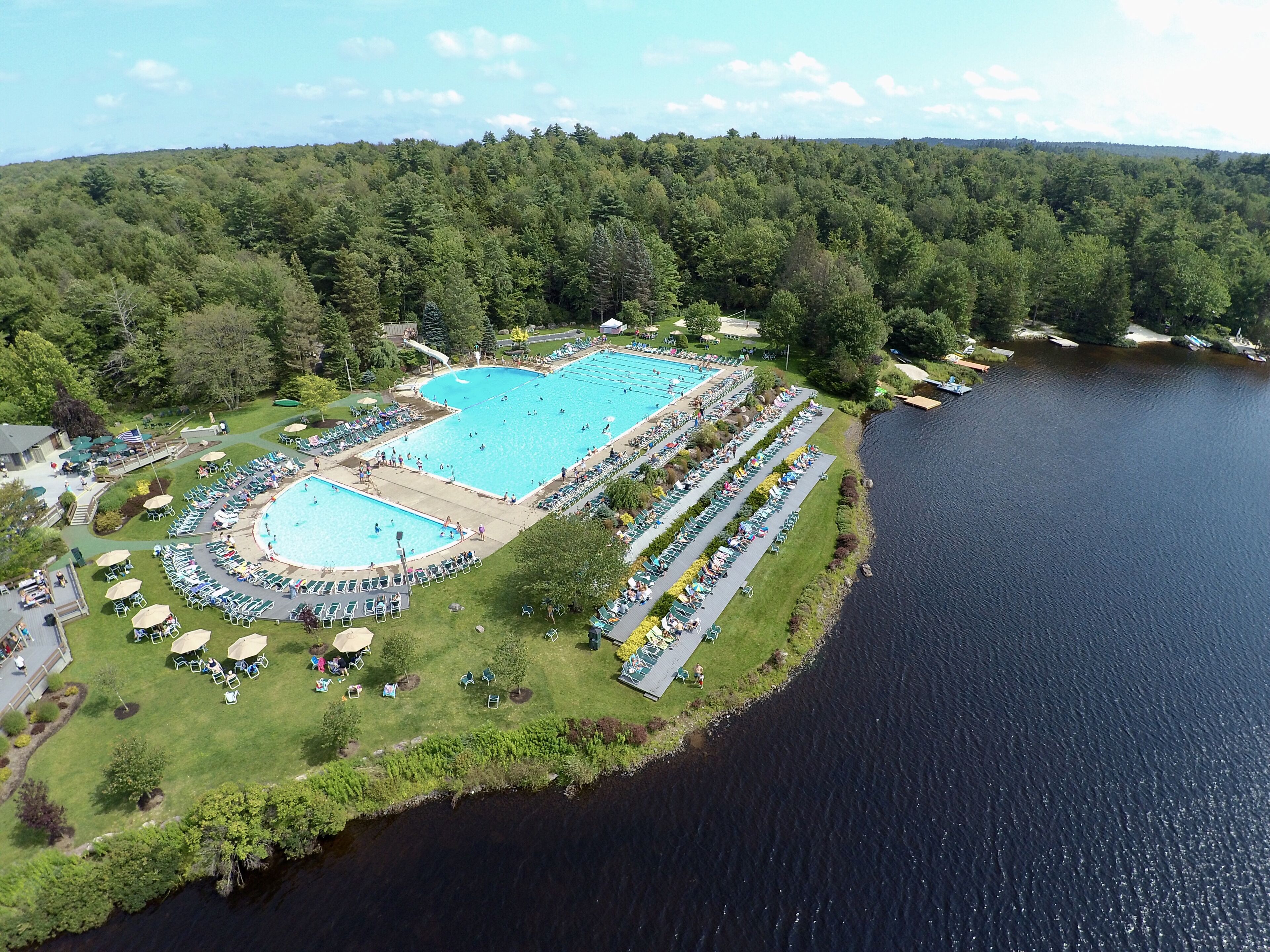 Luchtbeeld van een resort met een groot zwembad, omringd door ligbedden en een meer.
