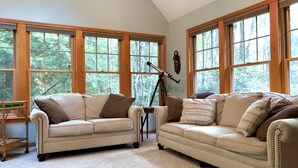 A living room with two beige sofas, a telescope, and large windows with a view of trees. - ⭐Central heat/AC ⭐ WiFi ⭐ Near pool, lake, beach!⭐ (Pocono Pines)