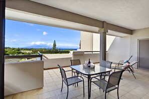A balcony with a table and chairs, a bottle of wine, and a view of the ocean and greenery.
