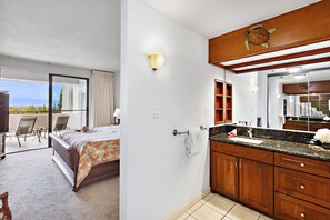 A bedroom with a large bed, a bathroom with wooden cabinets and a mirror, and a balcony with a view.