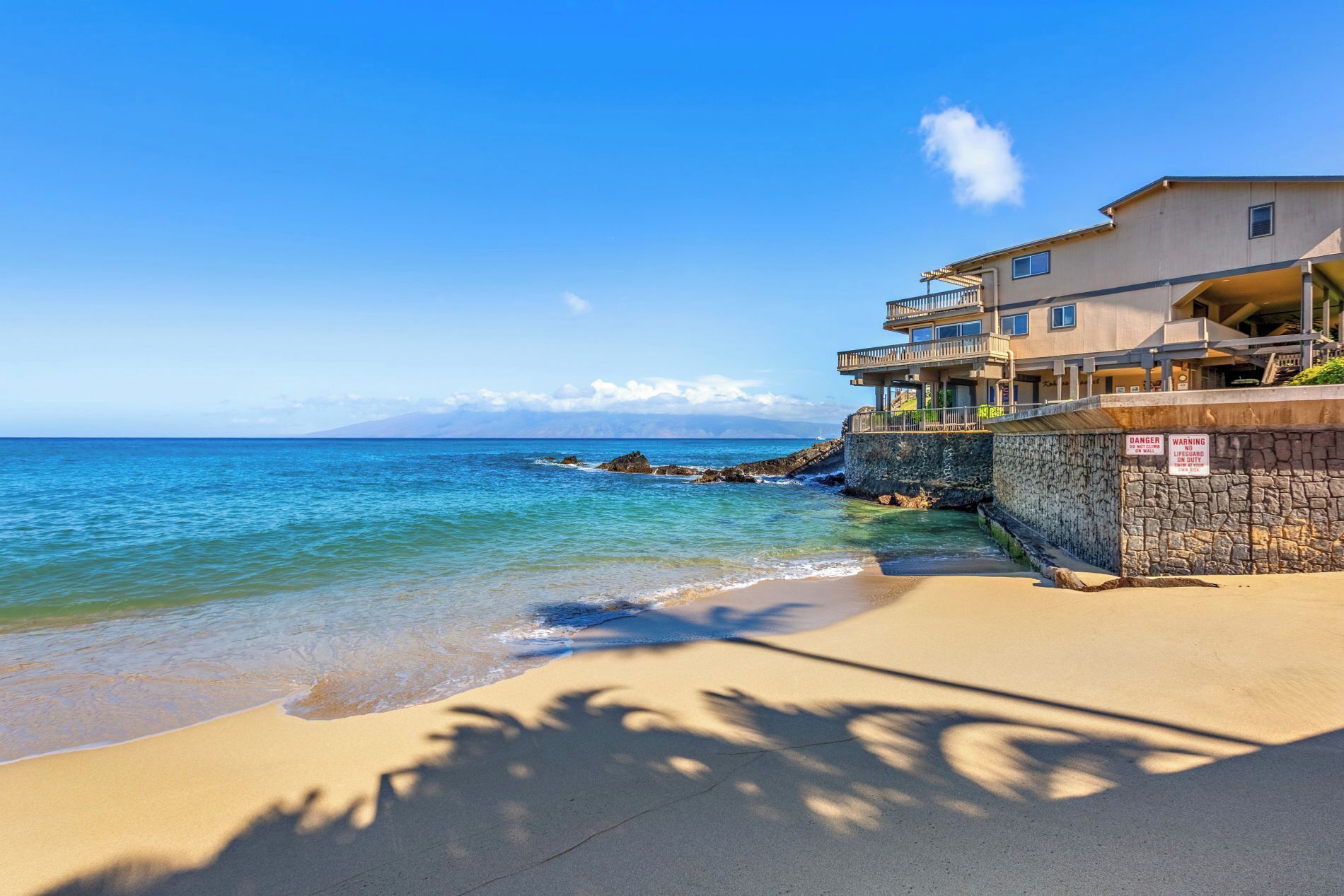 Un hotel amb vistes a la platja, façana de pedra, i un balcó amb vista a l'oceà.
