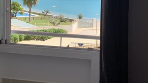 A room with a large window overlooking a pool, palm trees, and a mountainous coastline.