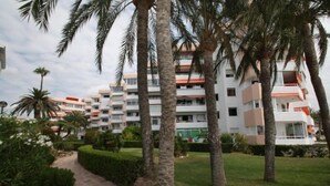 A multi-story hotel with balconies, surrounded by palm trees and a well-maintained garden.