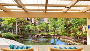 A covered outdoor area with wicker chairs, a small pond, and lush tropical plants. - Lock in your Maui Escape - Oceanfront, AC, 3bd -SK356-Sullivan Properties (Lahaina)