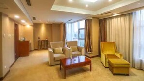 Une chambre d’hôtel comprenant un canapé, un fauteuil et un pouf disposés autour d’une table basse centrale.
