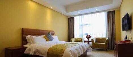 A hotel room with a large bed, a desk, two chairs, and a TV on the wall.