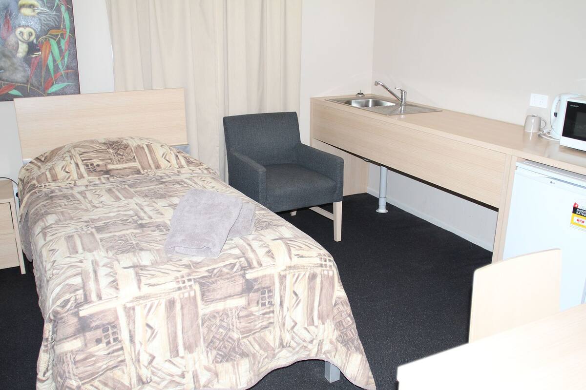 A hotel room with a bed, a chair, a desk with a sink, and a microwave.