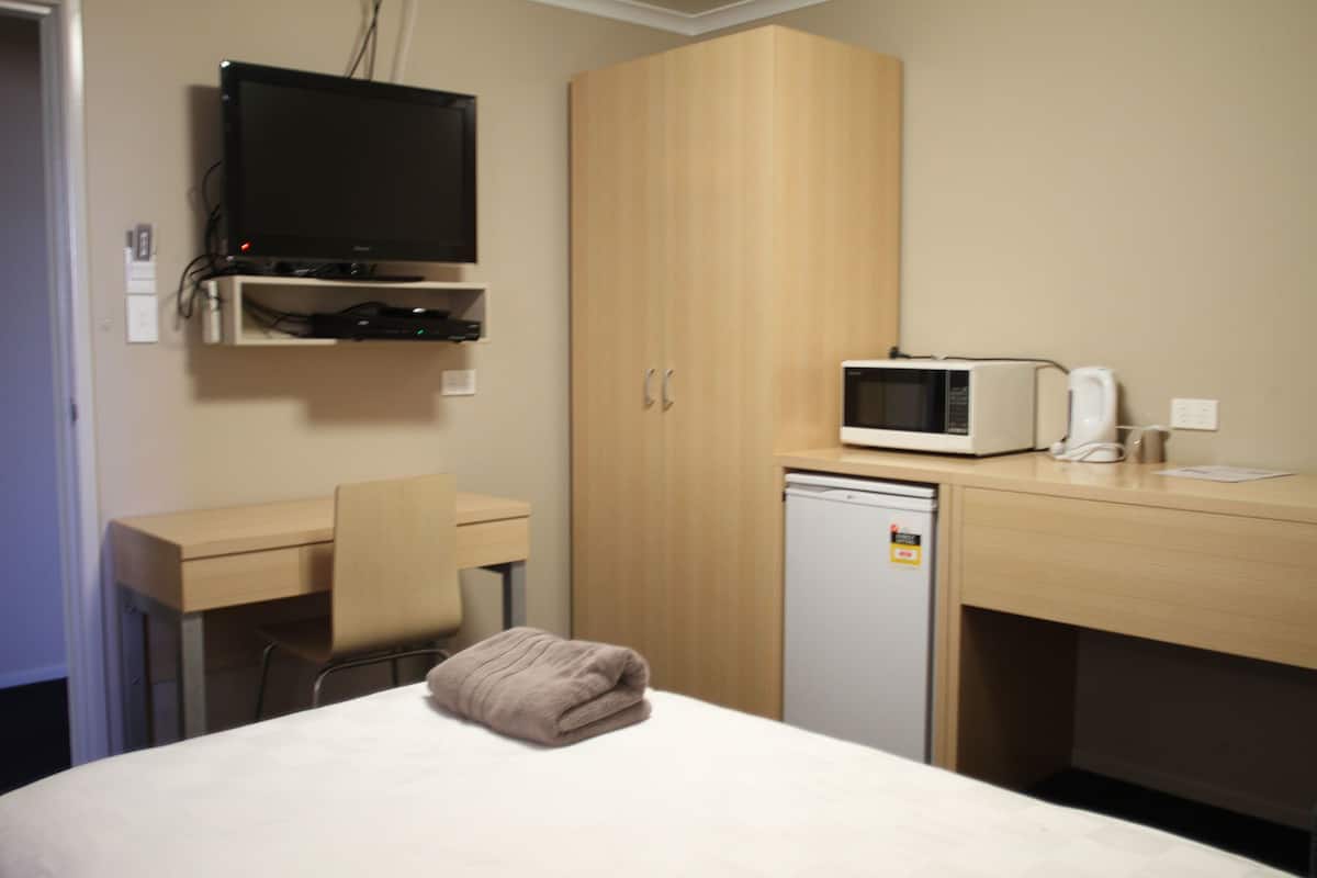 A hotel room with a bed, a desk, a television, a microwave, and a small refrigerator.