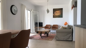 Un salon moderne comprenant un coin repas, un canapé, deux fauteuils, une table basse, un téléviseur et un tableau au mur.