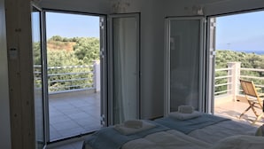 Une chambre avec deux lits, un balcon doté d’une balustrade blanche, et une vue sur la verdure et la mer.