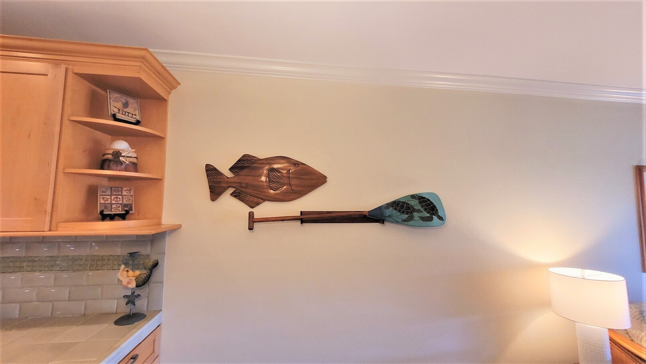 A kitchen with wooden cabinets, a fish-shaped wall hanging, and a wall-mounted paddle.