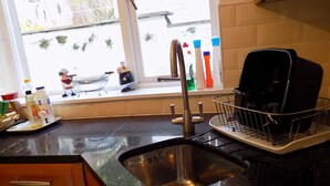 Une cuisine dotée d’un évier en acier inoxydable, d’une fenêtre donnant sur l’extérieur et de divers ustensiles de cuisine disposés sur le plan de travail.