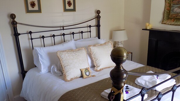 Un lit bien fait, recouvert d’une courtepointe matelassée, agrémenté de deux coussins décoratifs et surmonté d’une petite table de chevet avec une lampe.