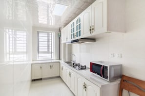 Eine moderne Küche mit weißen Schränken, einer Mikrowelle und einem Fenster mit Jalousien.