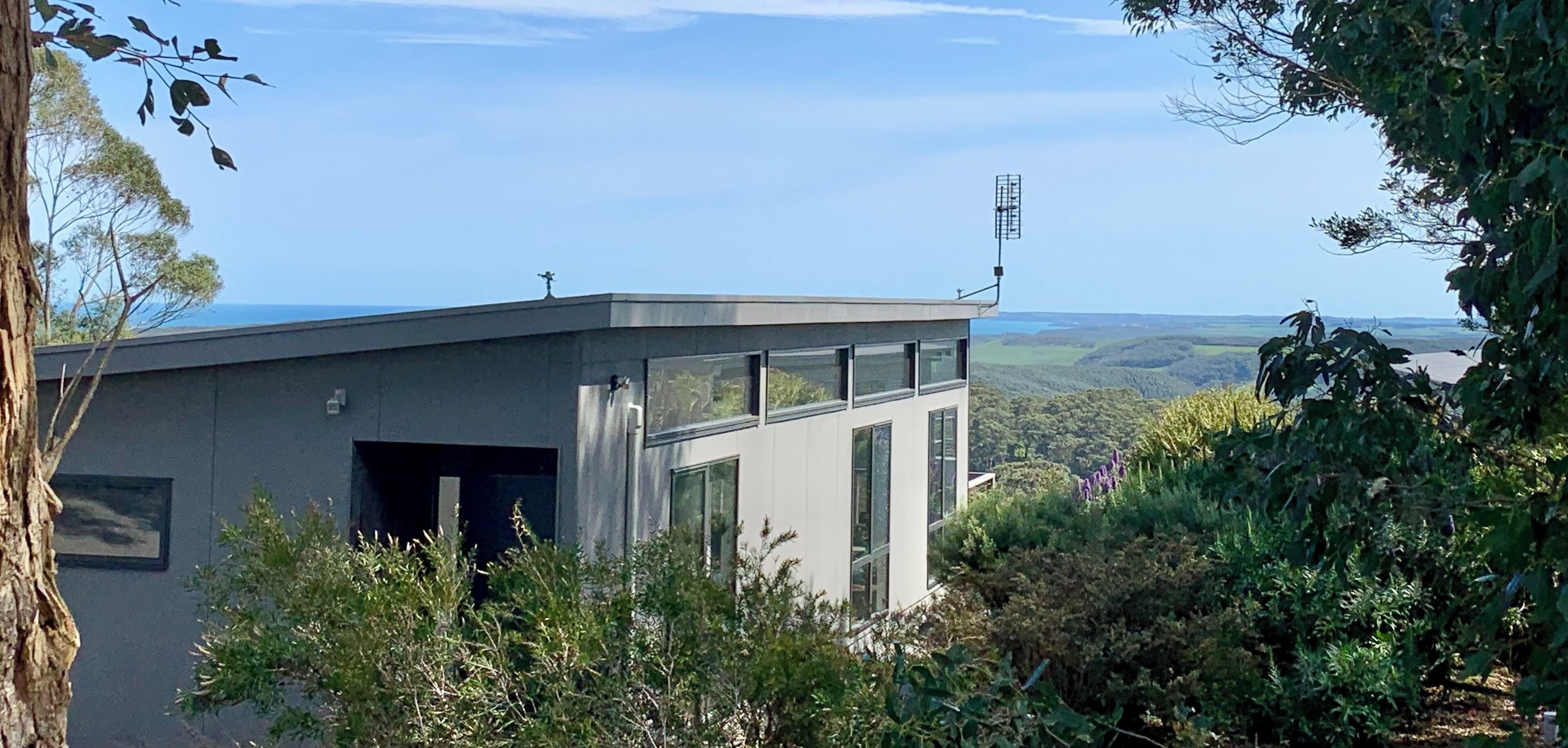 Un bâtiment moderne doté de grandes fenêtres, entouré d’une végétation luxuriante et offrant une vue dégagée sur le paysage.