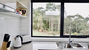Eine moderne Küche mit weißen Fliesen, einem Toaster, einem Wasserkocher und einem Spülbecken mit Blick auf einen Wald durch ein großes Fenster.