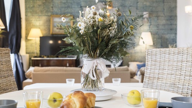 Morgenmad med en vase blomster, et fad med kager og glas appelsinjuice på et bord.