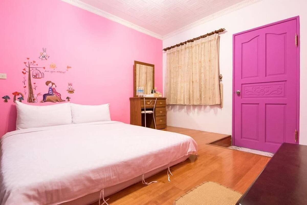 A bedroom with a pink wall, a wooden bed, a purple door, and a window with curtains.