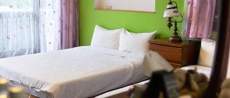 A neatly made bed in a room with a green wall, a wooden nightstand, and a lamp.