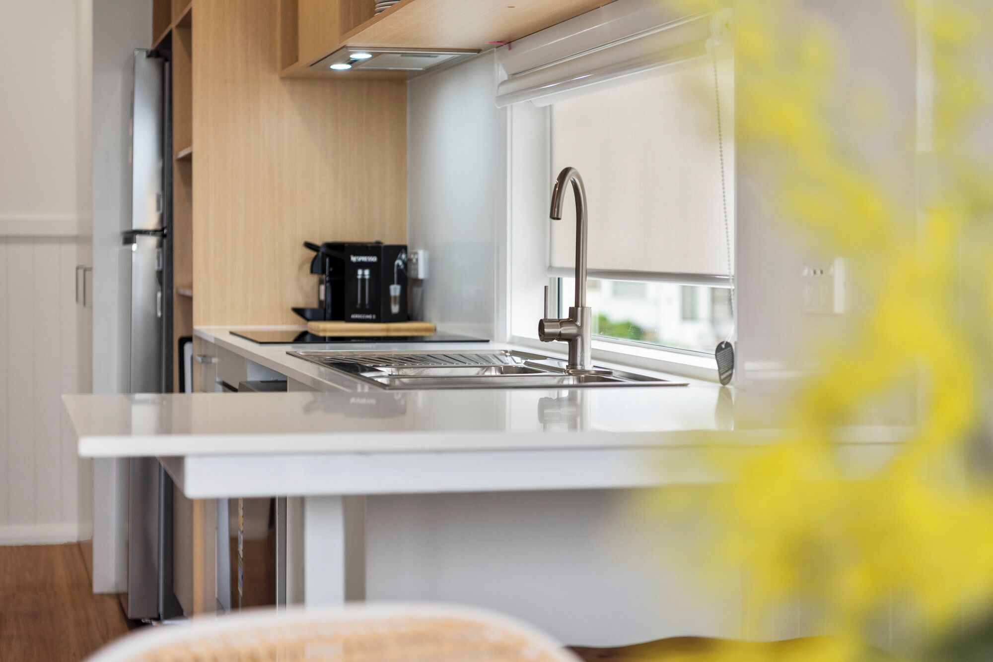 A modern kitchen with a stainless steel sink, a coffee machine, and wooden cabinets.