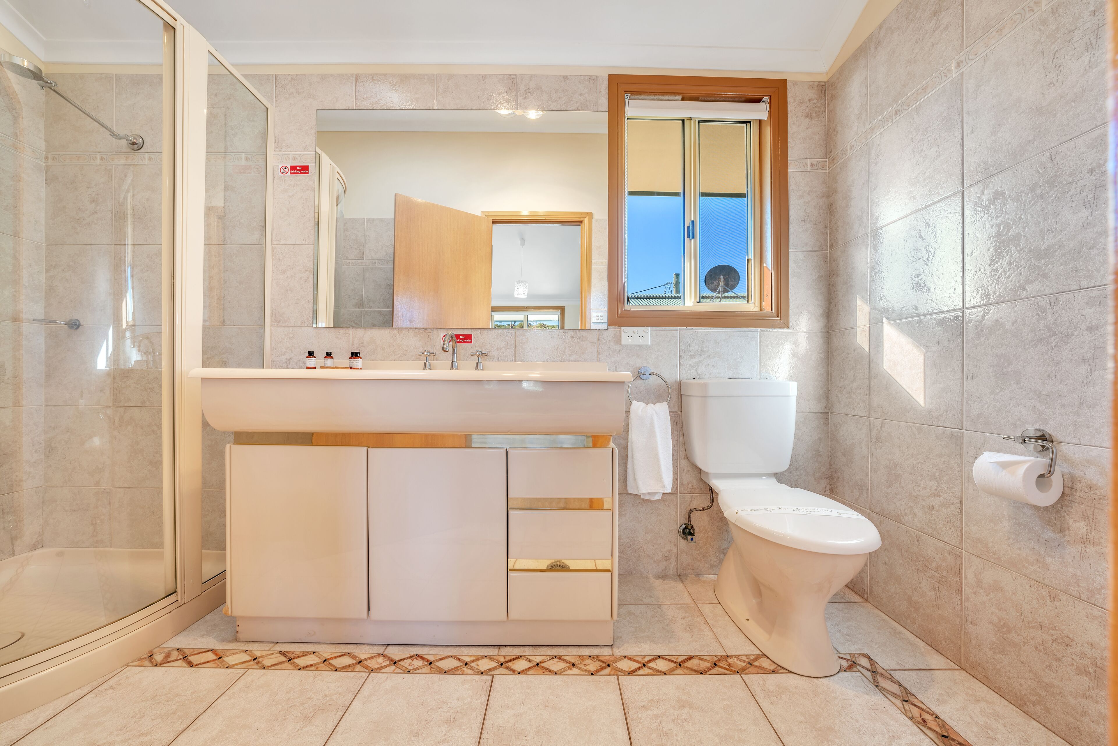 Een moderne badkamer met een douchecabine van glas, een wit wastafelmeubel met een spiegel erboven en een toilet met een raam erboven.