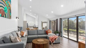 Una sala moderna con un sofá seccional gris, una mesa de centro de madera y un ventanal con vistas al exterior.