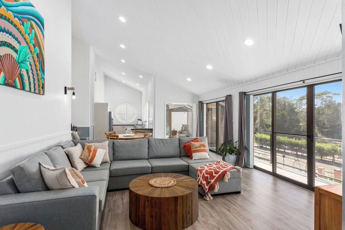 Una sala moderna con un sofá seccional gris, una mesa de centro de madera y un ventanal con vistas al exterior.