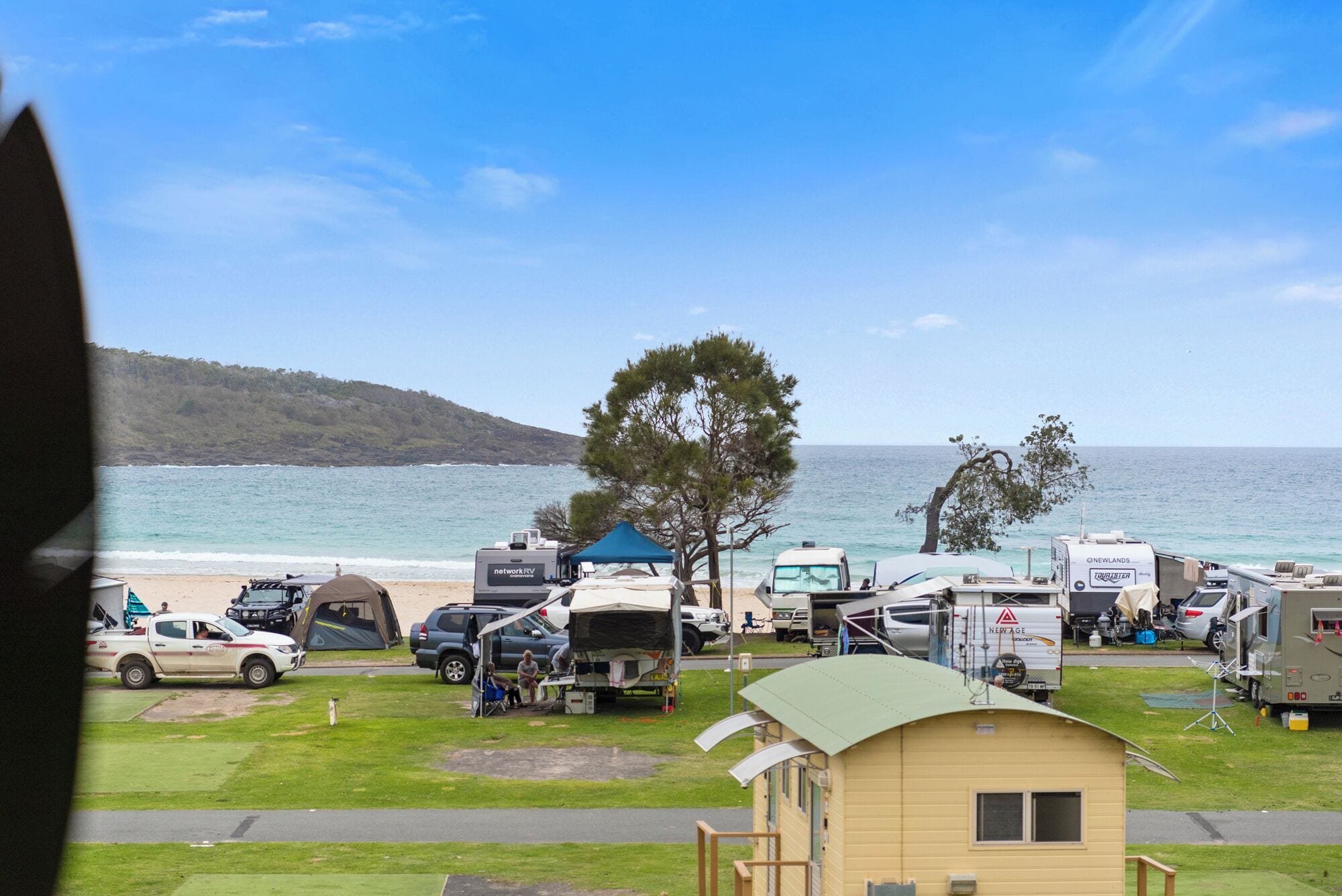 A campsite with RVs and tents by the sea, a small yellow building, and a clear view of the ocean.