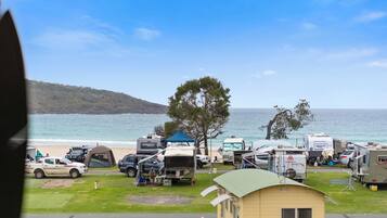 A campsite with RVs and tents by the sea, a small yellow building, and a clear view of the ocean.