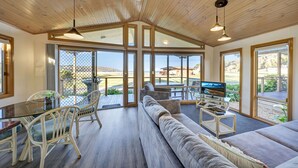 Amplia sala de estar con un sofá grande, mesa de comedor y sillas, televisor y ventanas grandes que ofrecen vistas al exterior.