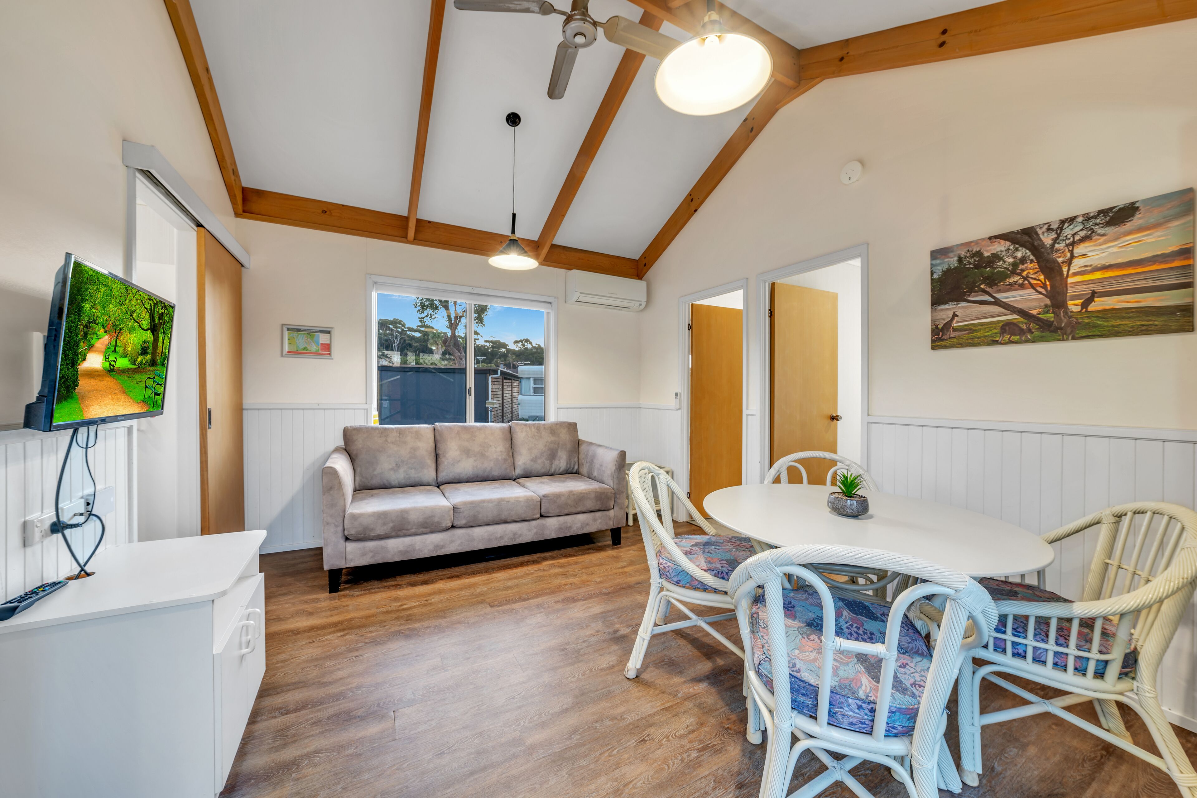 A cozy room with a wooden ceiling, a sofa, a dining table with chairs, and a painting on the wall.