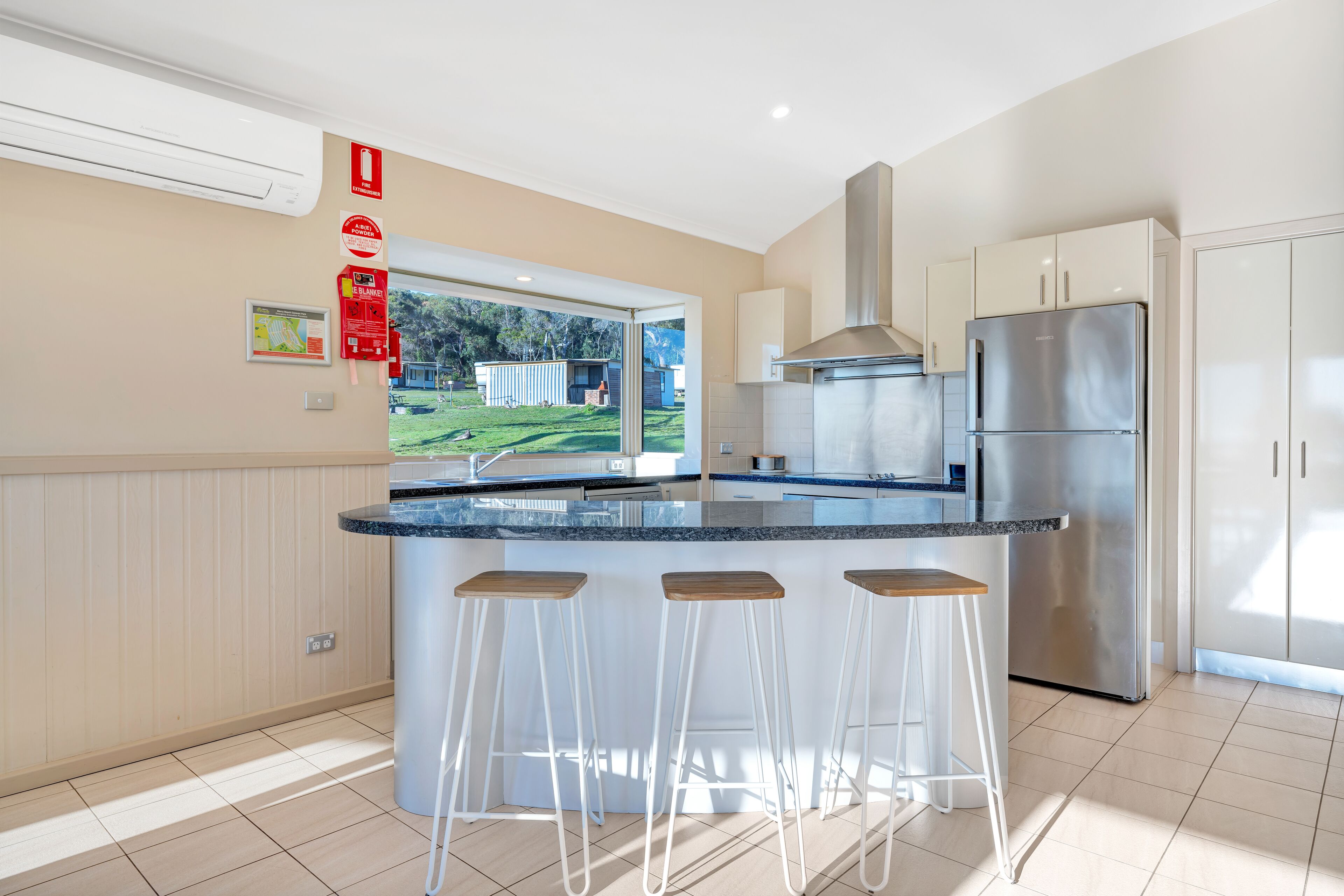 A modern kitchen with a central island, stainless steel appliances, and a view of the outdoors.