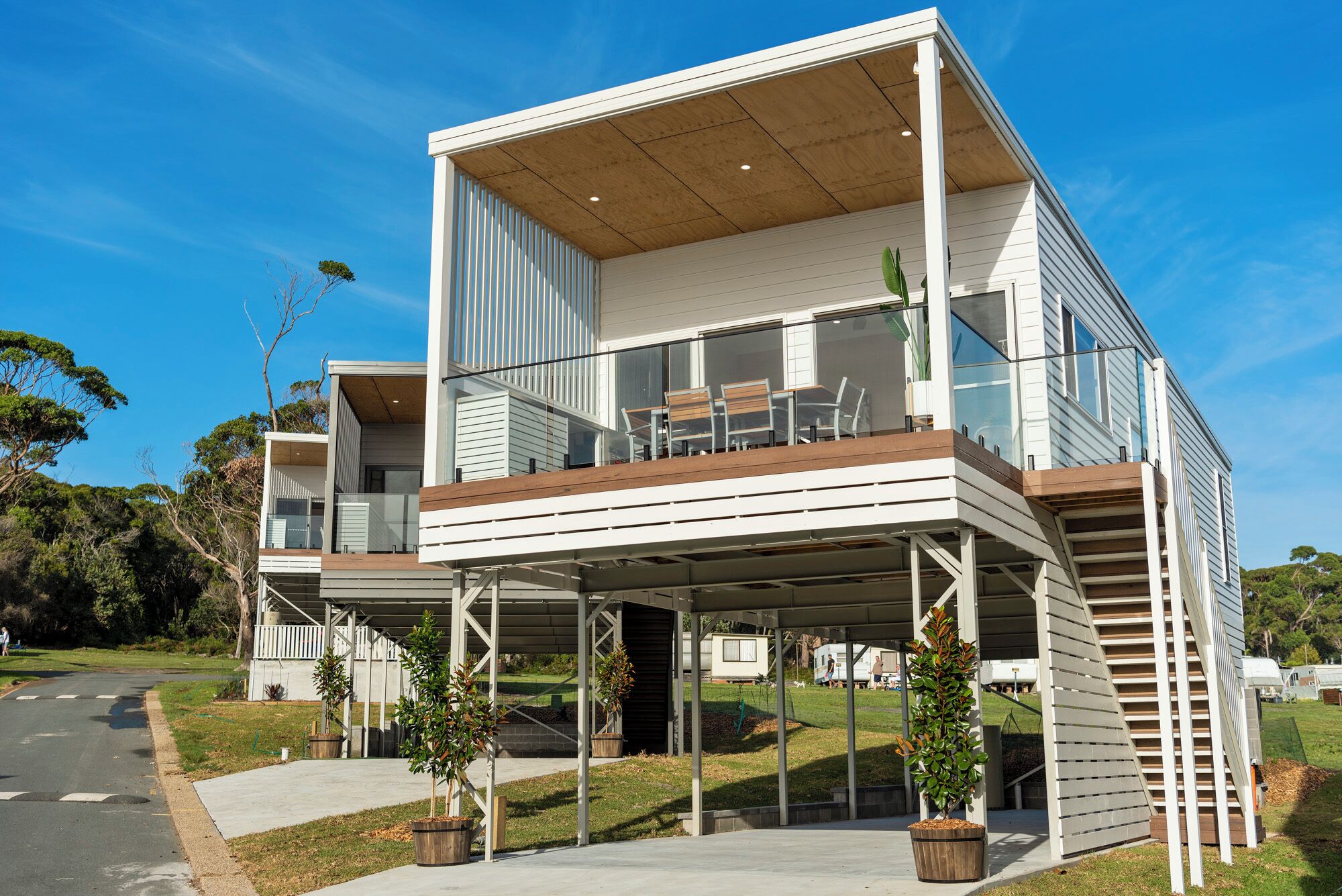 Una casa moderna de dos pisos con un patio cubierto, un balcón y un pequeño jardín con plantas en macetas.