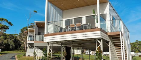 Una casa moderna de dos pisos con un patio cubierto, un balcón y un pequeño jardín con plantas en macetas.