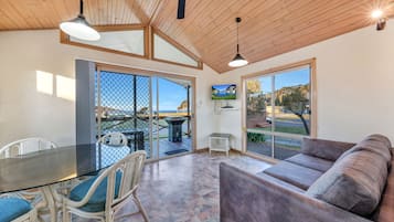 A spacious room with a glass table, wicker chairs, a cushioned sofa, and large windows offering a view of the outdoors.
