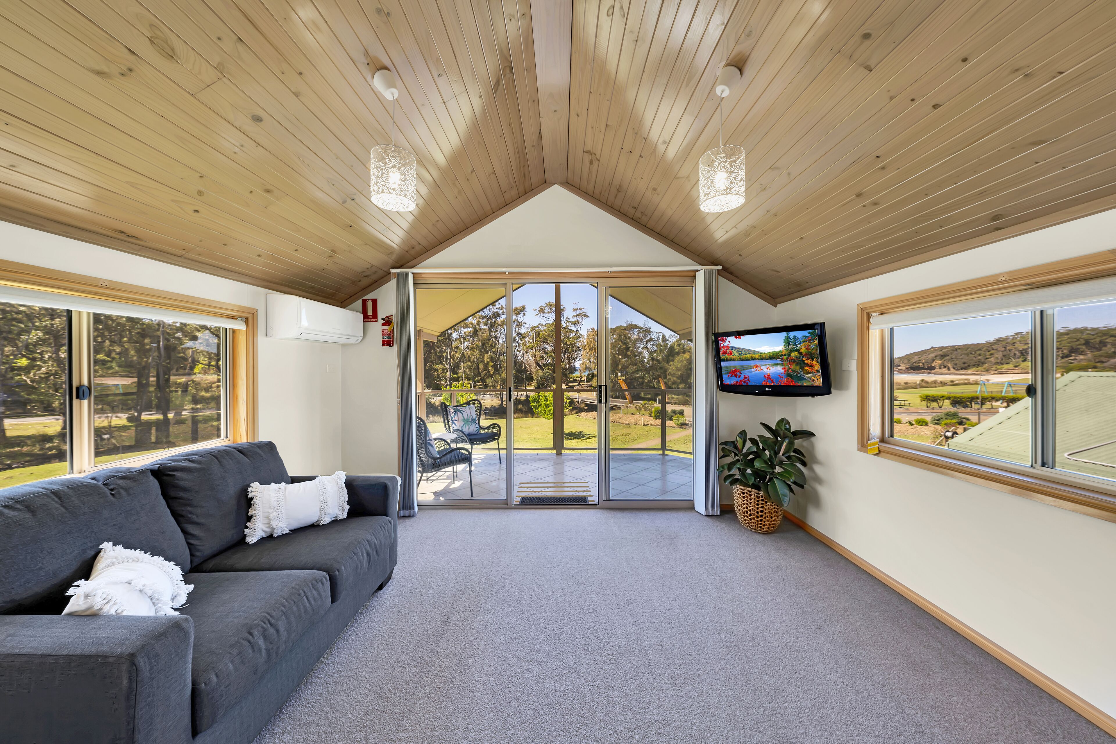 A modern interior with a grey sofa, a television, and a large sliding glass door leading to an outdoor area.
