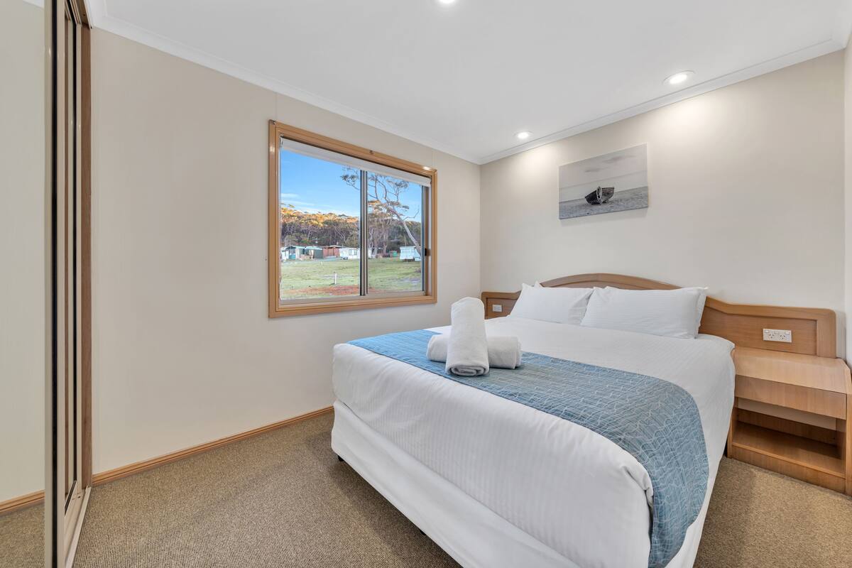 Habitación de hotel con una cama grande, una ventana con vistas al exterior, un cabecero de madera y una mesita de noche de madera.
