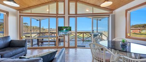Amplia sala de estar con un gran ventanal que da a un patio exterior, un espacio de estar confortable y un televisor sobre una mesa de vidrio.
