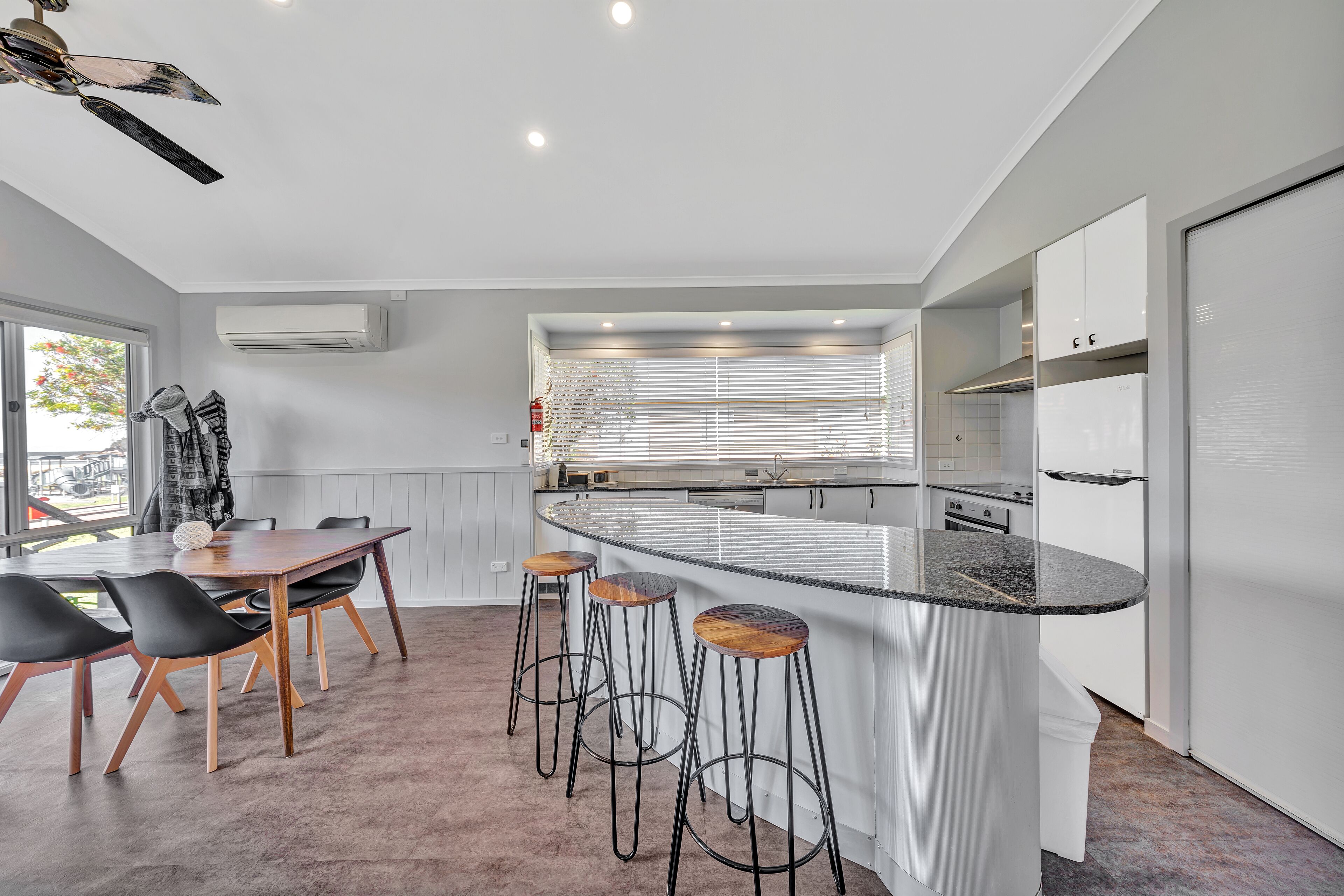 A modern kitchen with a central island, bar stools, and a dining area with a table and chairs.