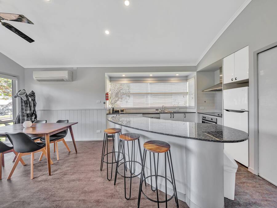 A modern kitchen with a central island, bar stools, and a dining area with a table and chairs.