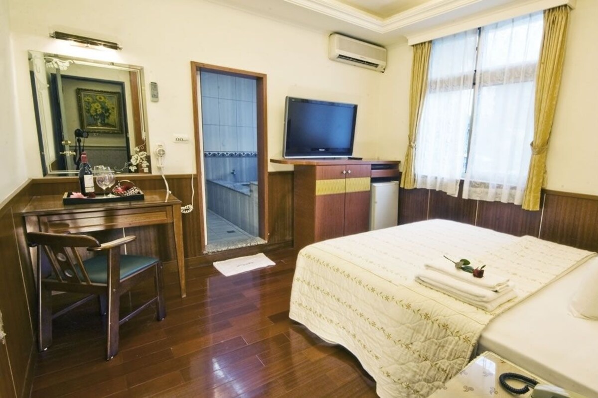 A hotel room with a bed, a desk with a chair, a television, and a small refrigerator.