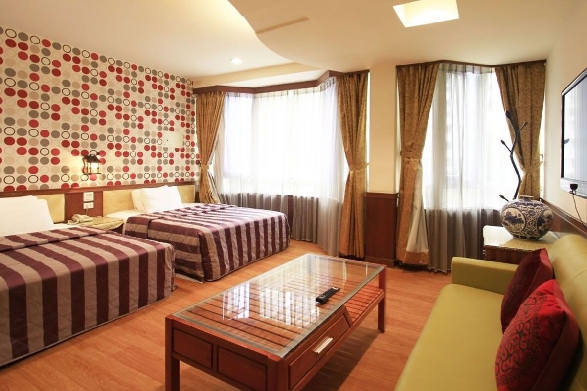 A hotel room with two beds, a sofa, a glass-top coffee table, and a TV.