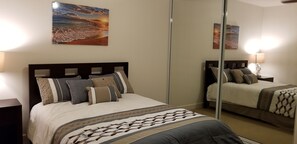 Une chambre à coucher comprenant un lit, une table de chevet, un miroir et un tableau accroché au mur.
